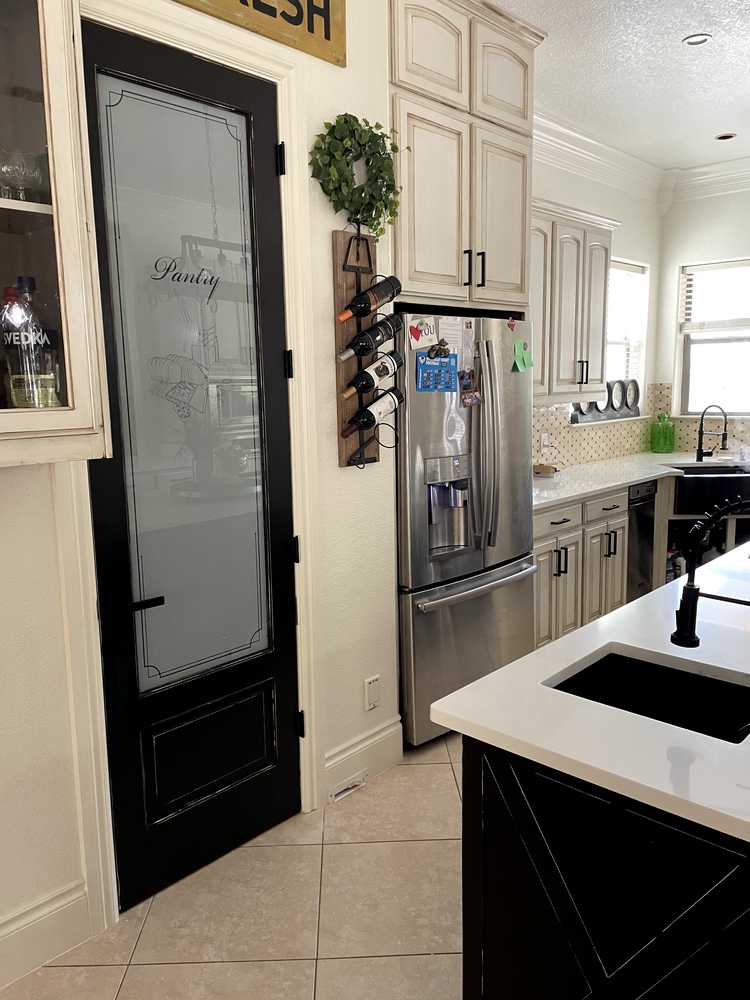Bright kitchen with stainless steel fridge, black pantry door, cream cabinets, and white island counter.
