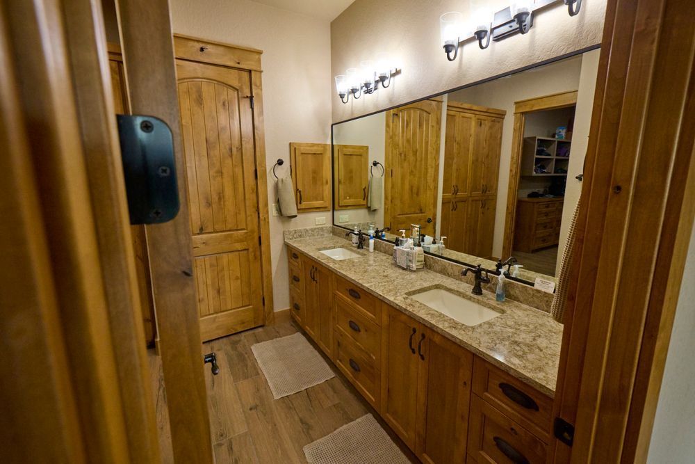 Wood-paneled bathroom with double vanity, large mirror, and rustic wooden door