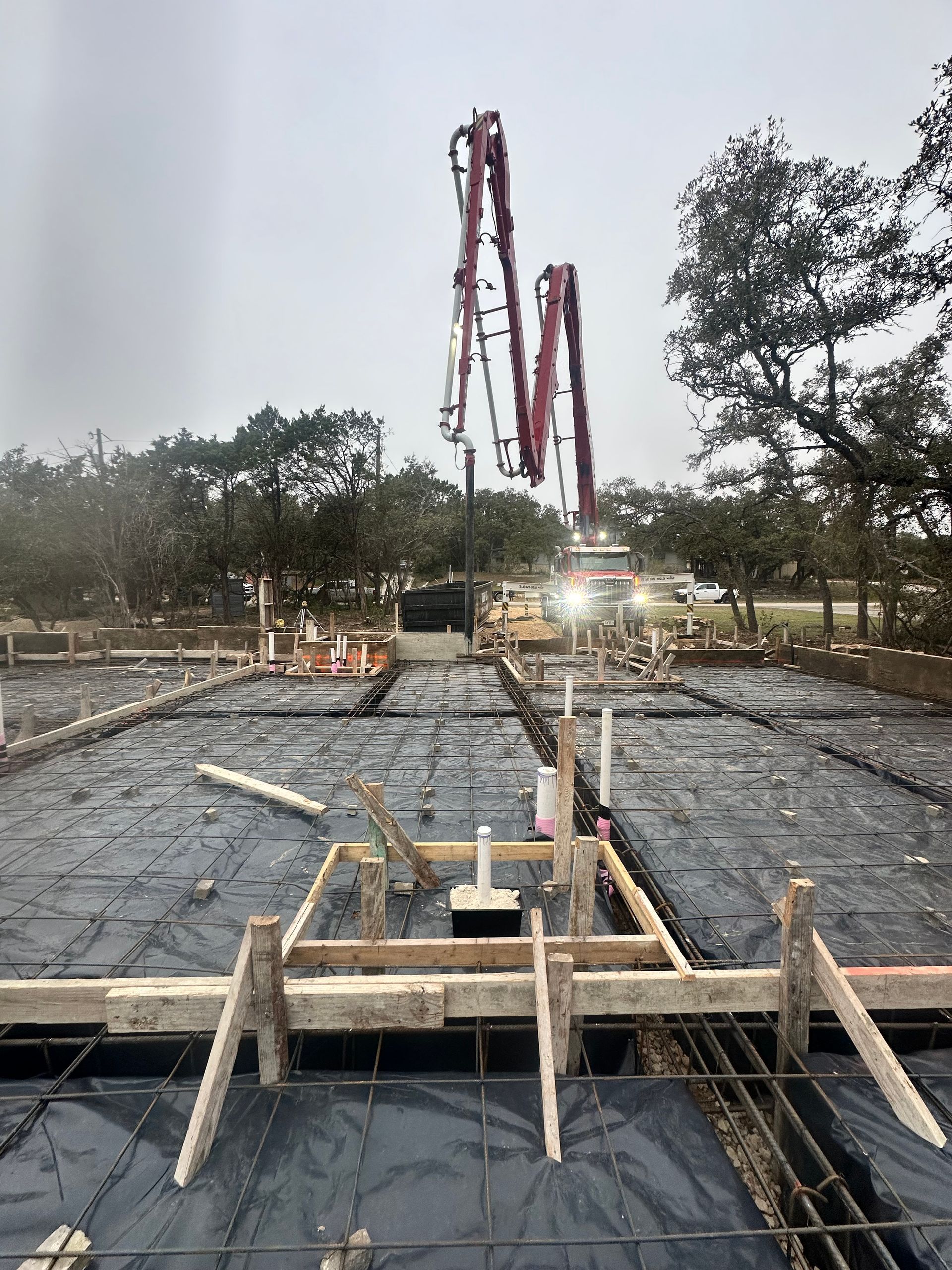 Concrete construction site with rebar and formwork, and a tall red boom pump in the background.