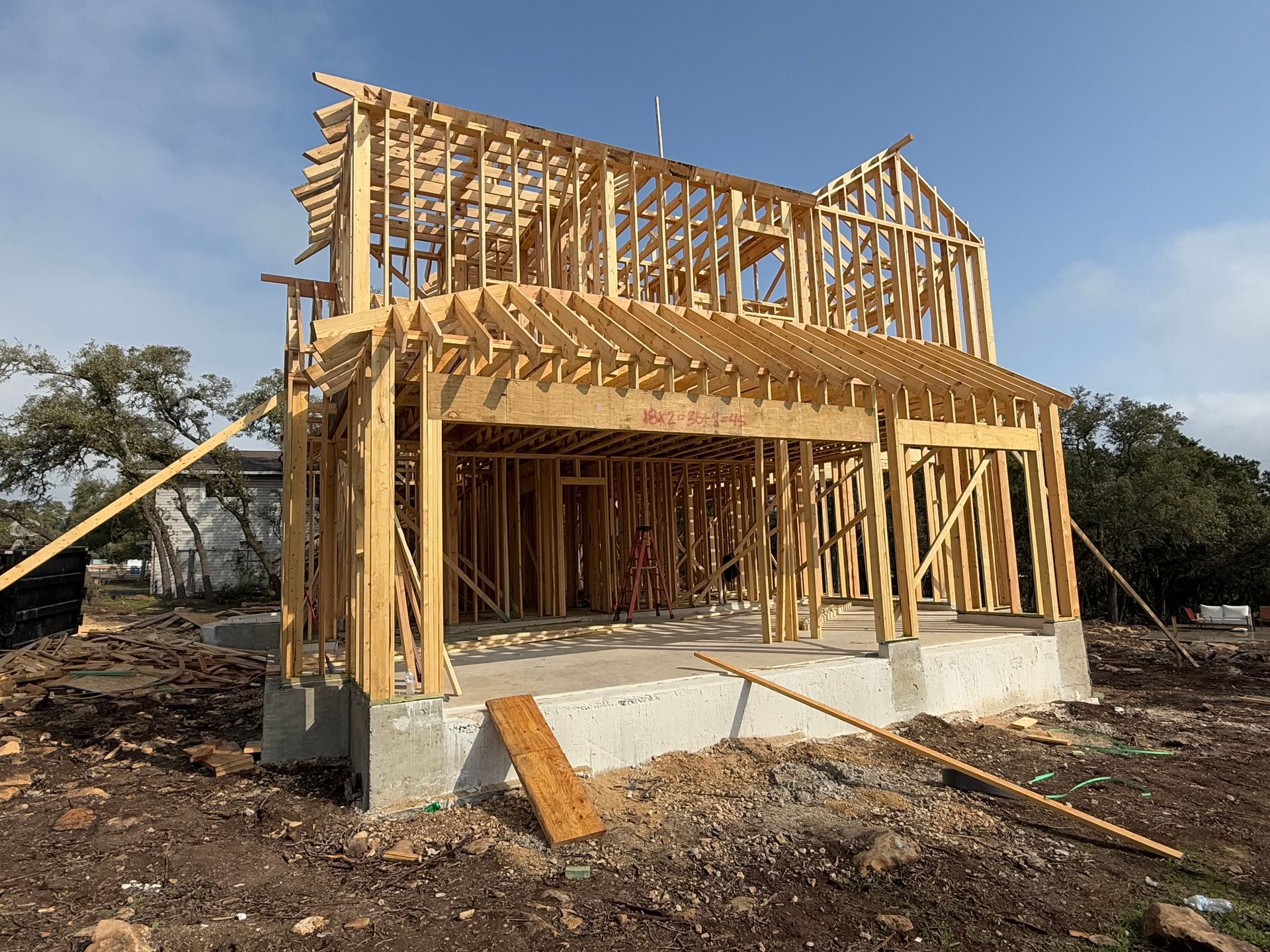 Partially framed house under construction with exposed wood beams and concrete foundation on a dirt lot