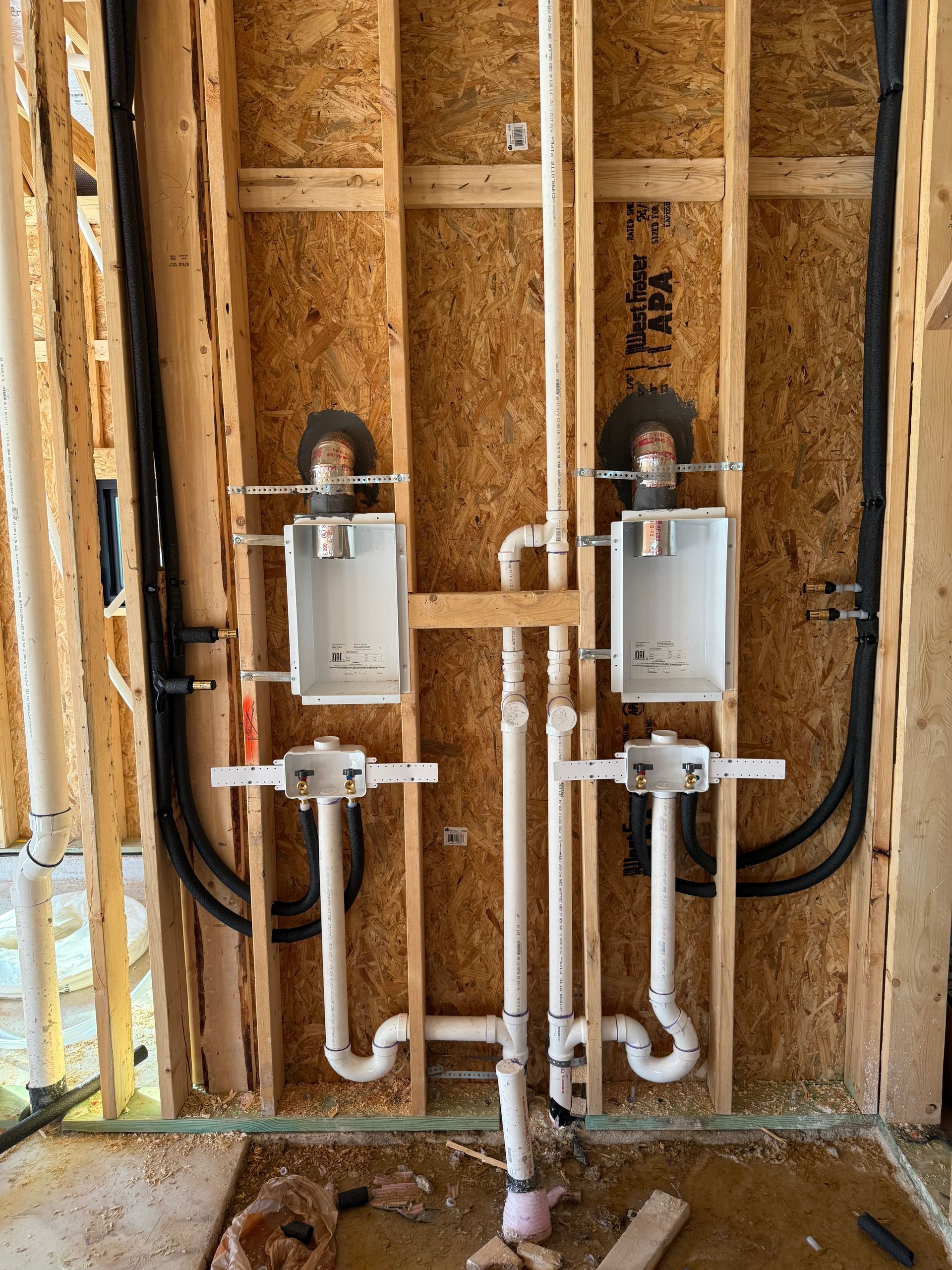 Two wall-mounted utility boxes with white pipes in an unfinished wood-framed wall
