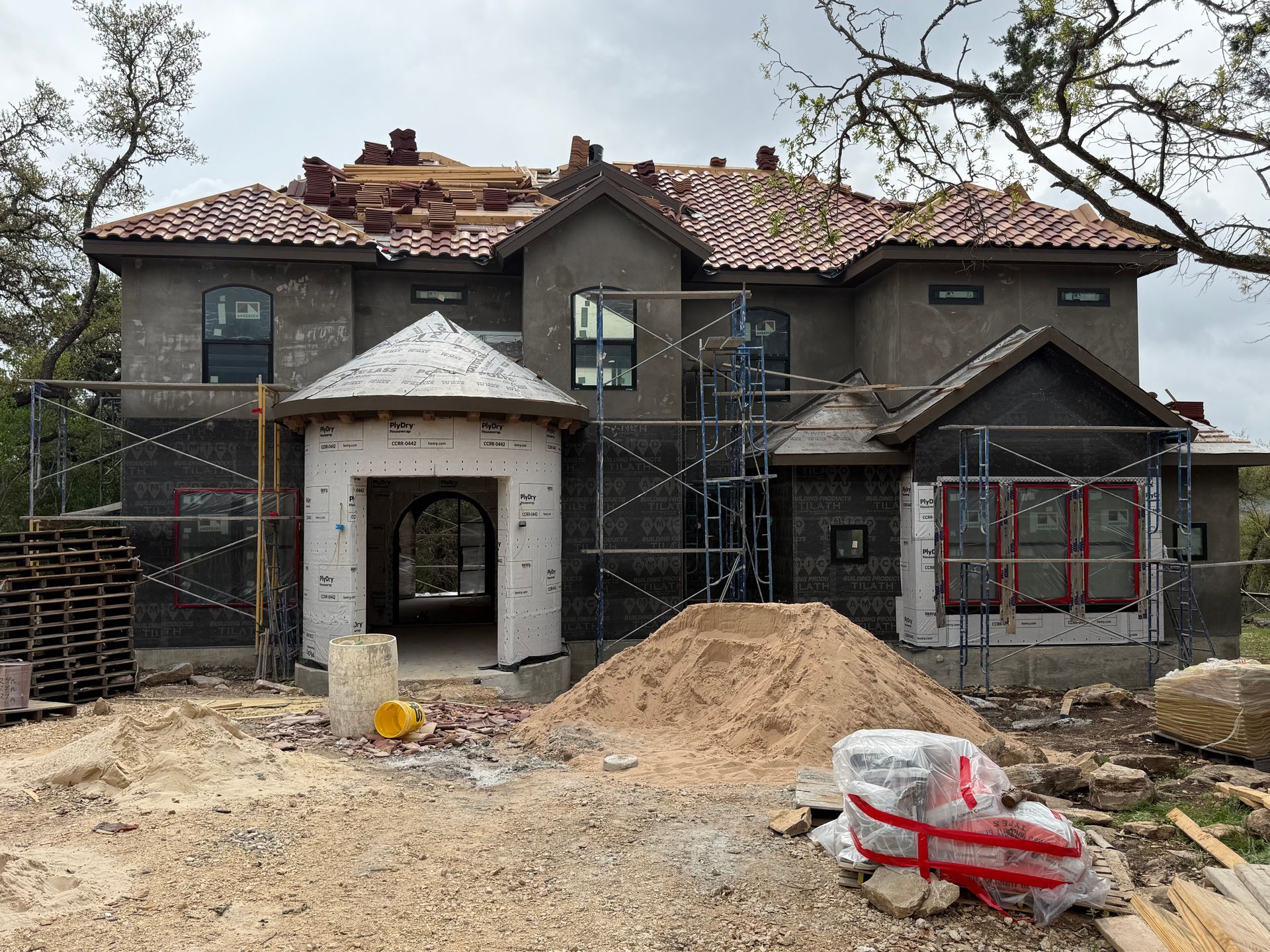 Two-story house under construction with scaffolding, roof tiles, and piles of dirt in front