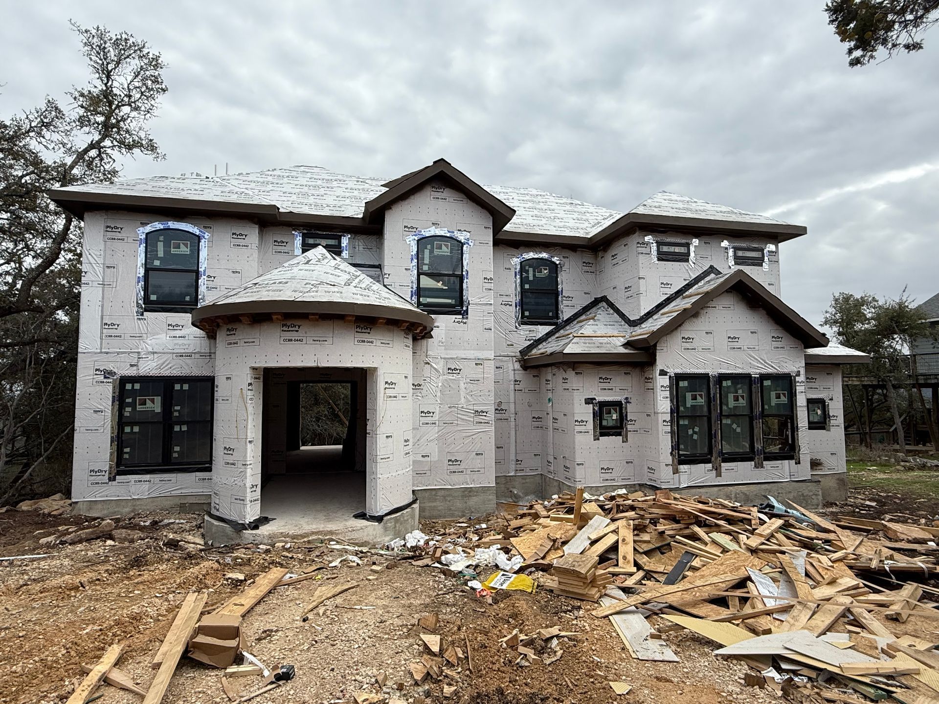 Two-story house under construction with white exterior and debris piled in the front yard