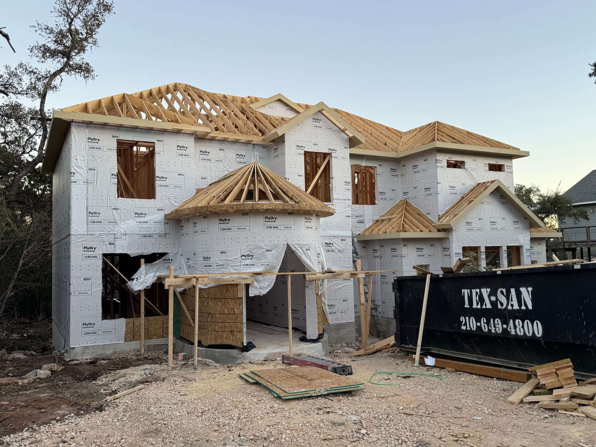 Partially built two-story white house with exposed roof framing and construction materials outside
