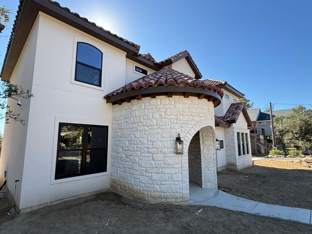 Modern two-story stucco house with white stone entry and red-tile roof under a clear blue sky