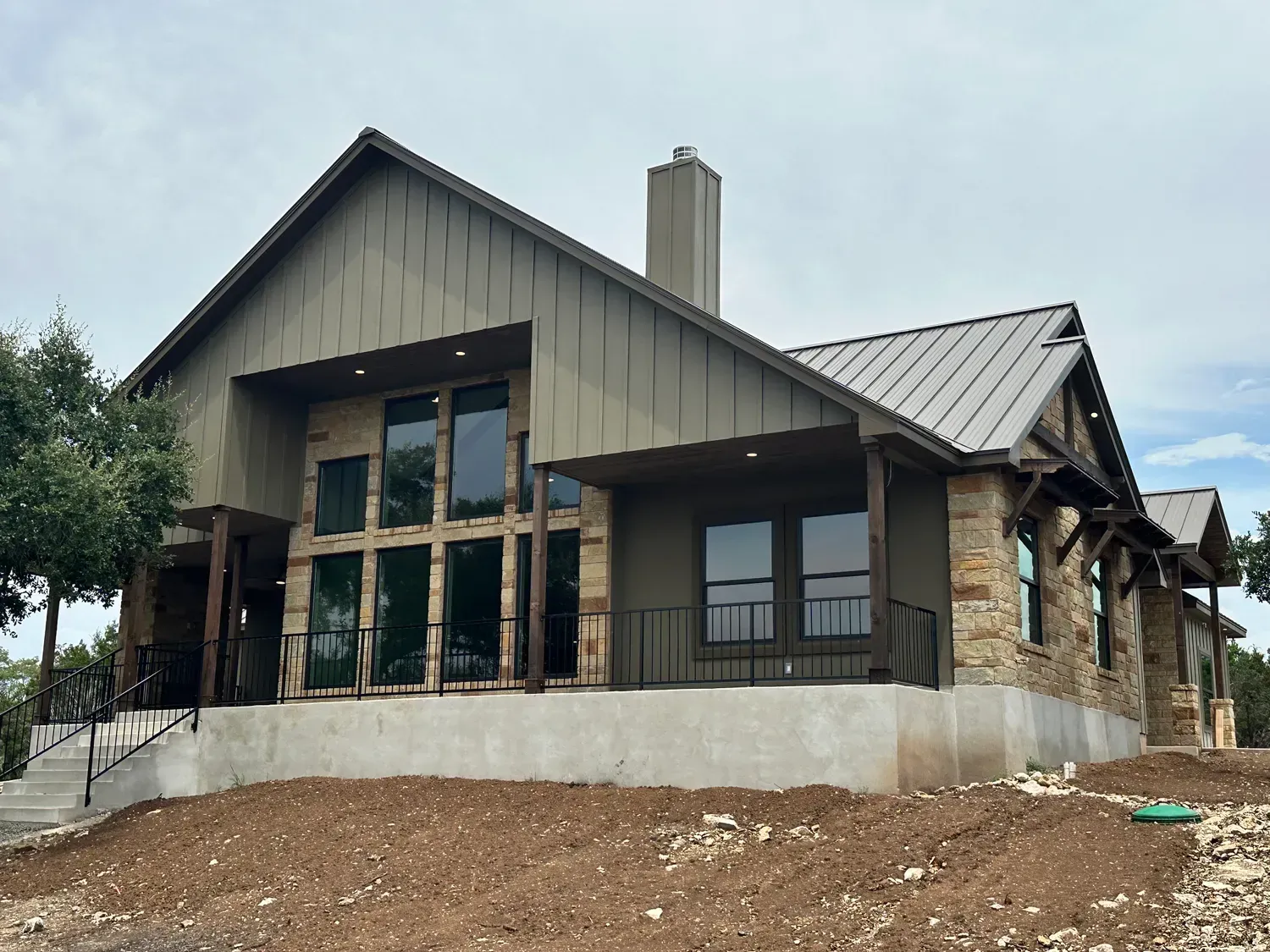 New house under construction with a gray metal roof and large front windows on a sloped lot