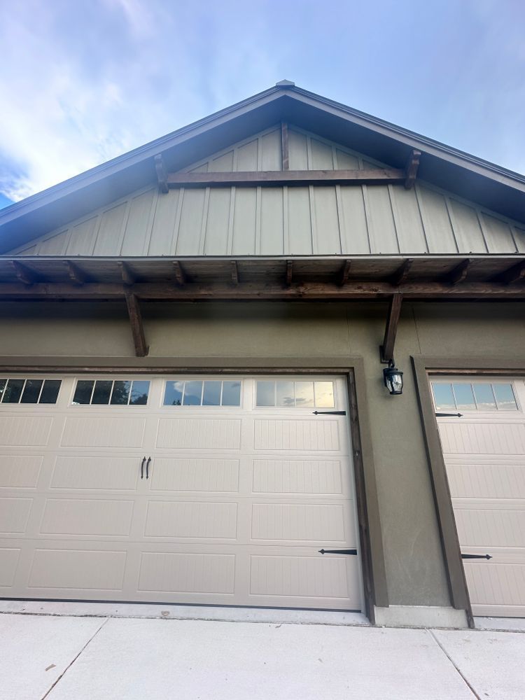 Single-story home exterior with a white garage door, gray siding, and snow on the driveway.