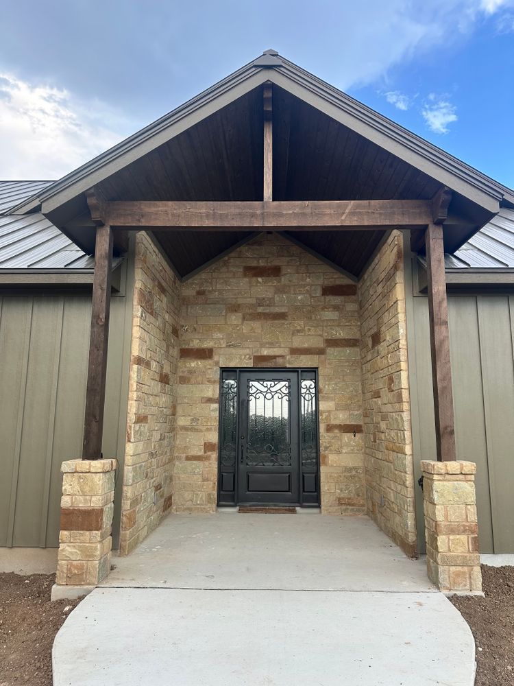 Front entrance with stone archway, black double doors, and wooden beams under a gabled roof.