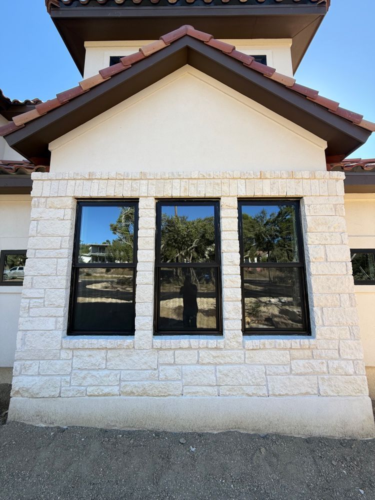 White stone building facade with three dark-framed windows and a peaked roof