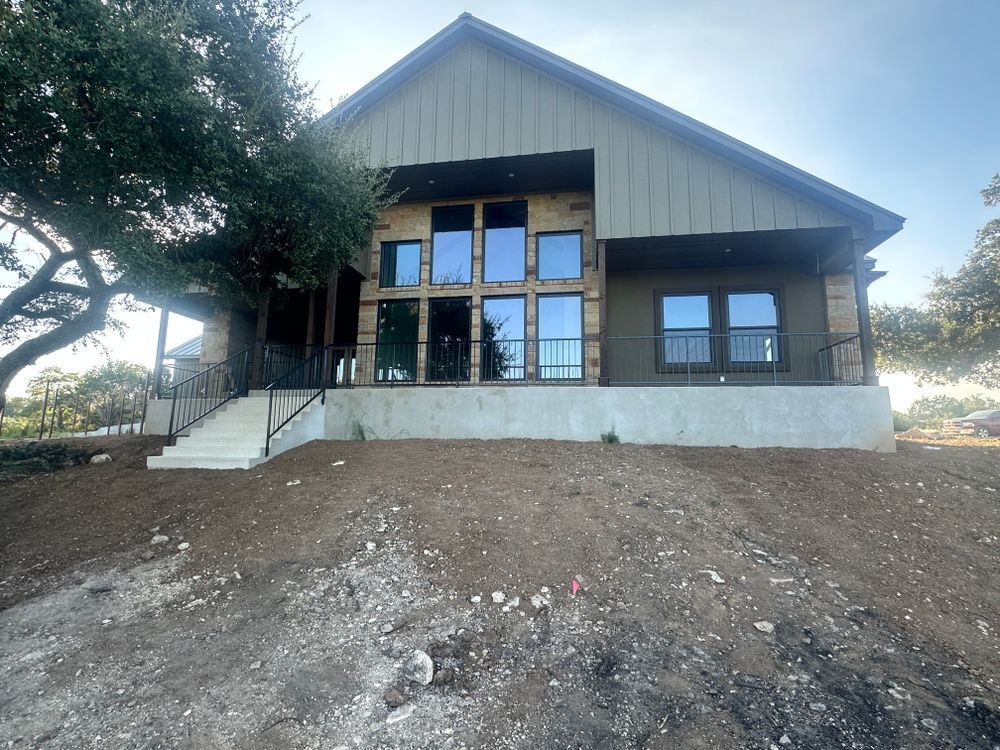Modern house with large windows, front steps, and a sloped dirt yard under trees