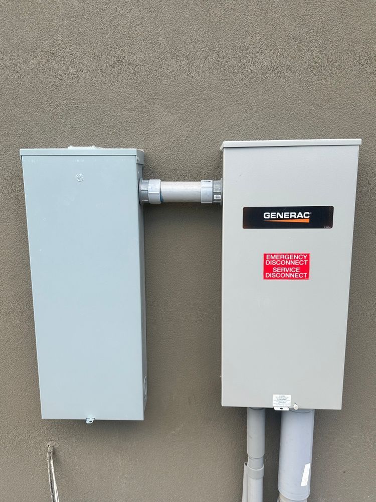 Two gray electrical panels mounted on a beige exterior wall, connected by conduit.