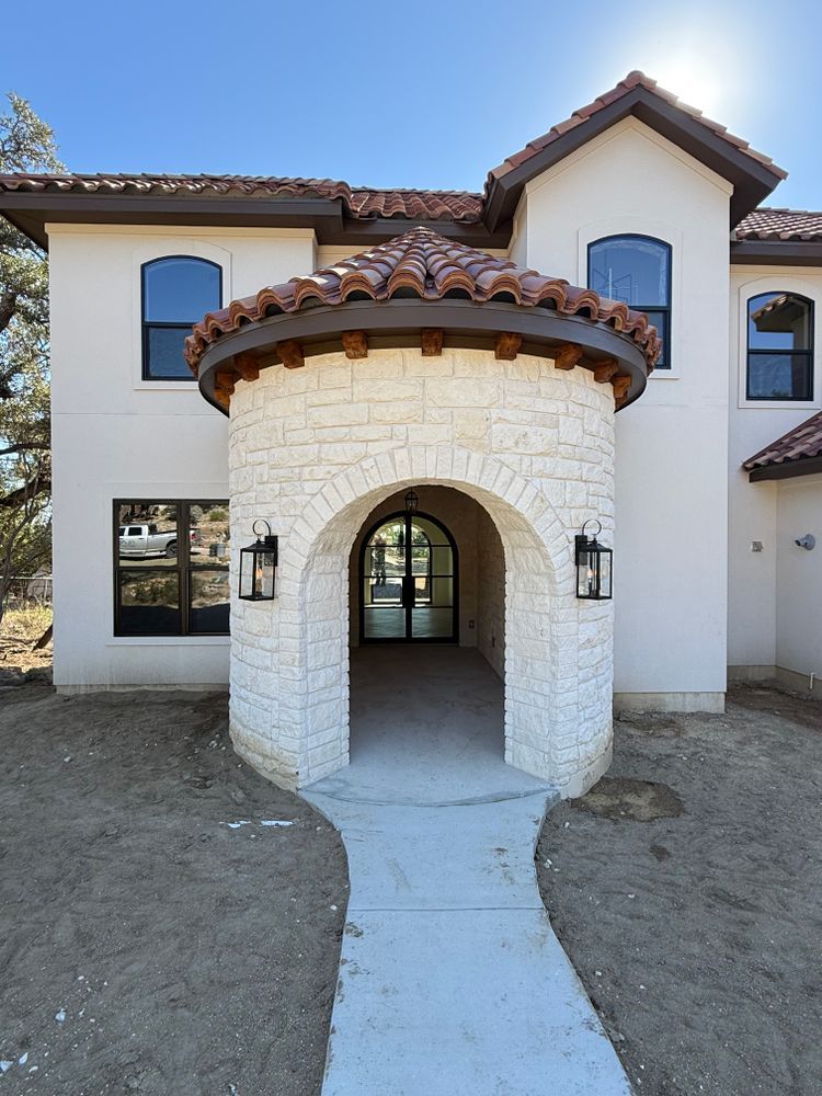 Mediterranean-style house entrance with white stucco and stone tower archway, front walkway centered on facade