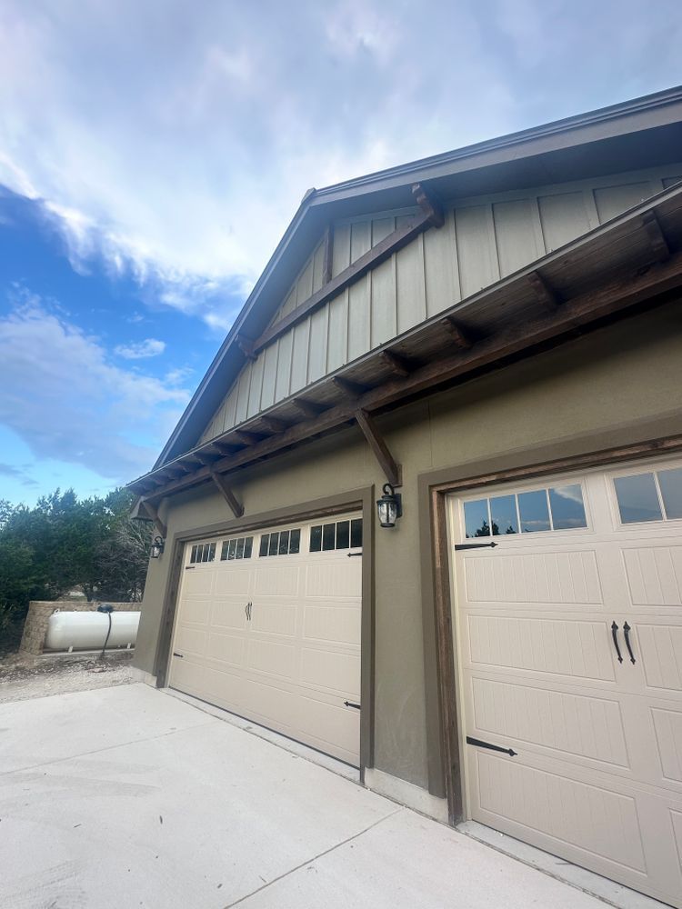 Two beige garage doors on a house exterior with a concrete driveway and blue sky above