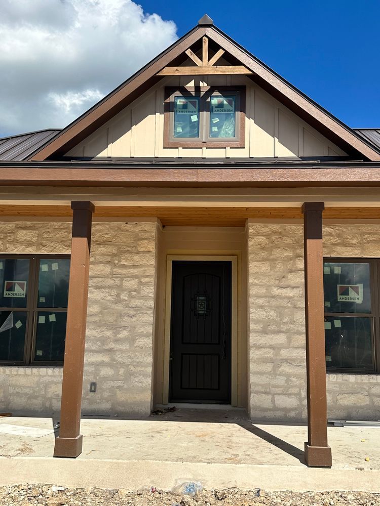 Front view of a tan stone house with a dark front door, porch columns, and a gabled roof under a blue sky