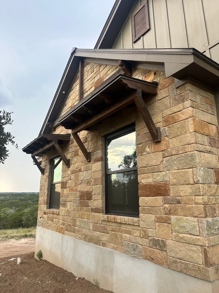 Stone house exterior with a black-framed window and rustic wooden gable awning