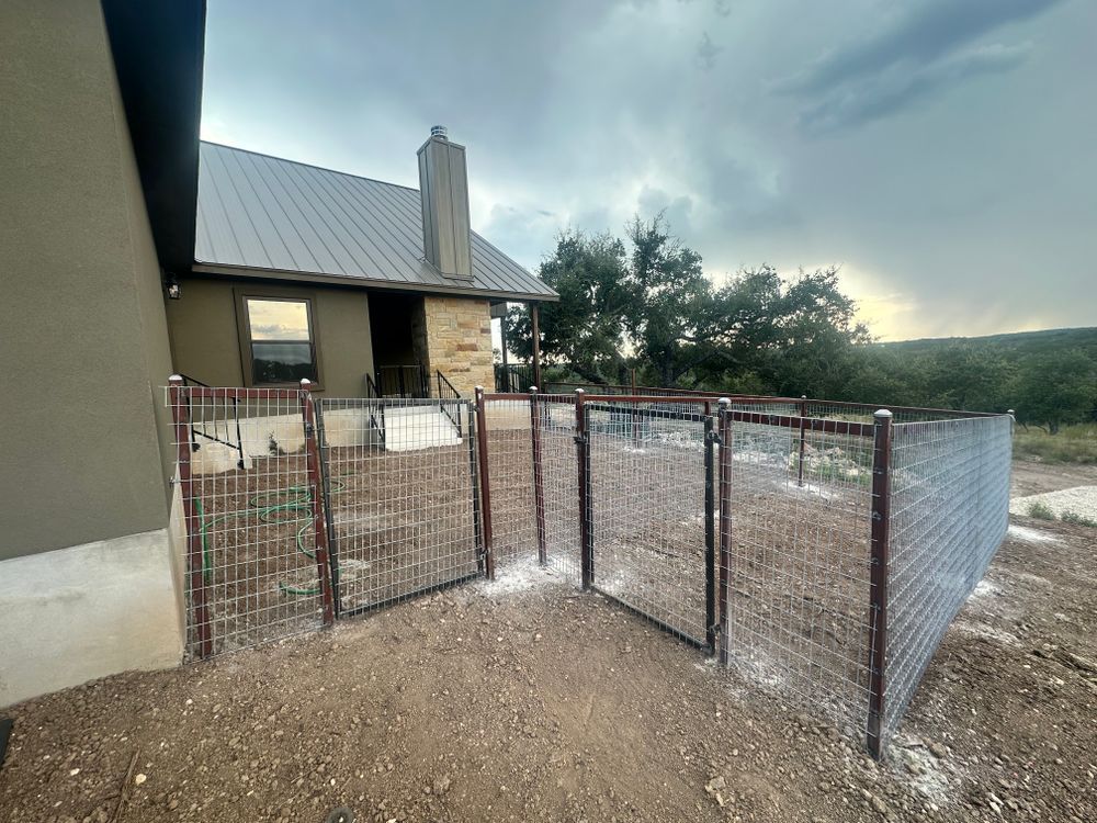 Wire-mesh fenced outdoor enclosure beside a house with gravel ground and cloudy sky.