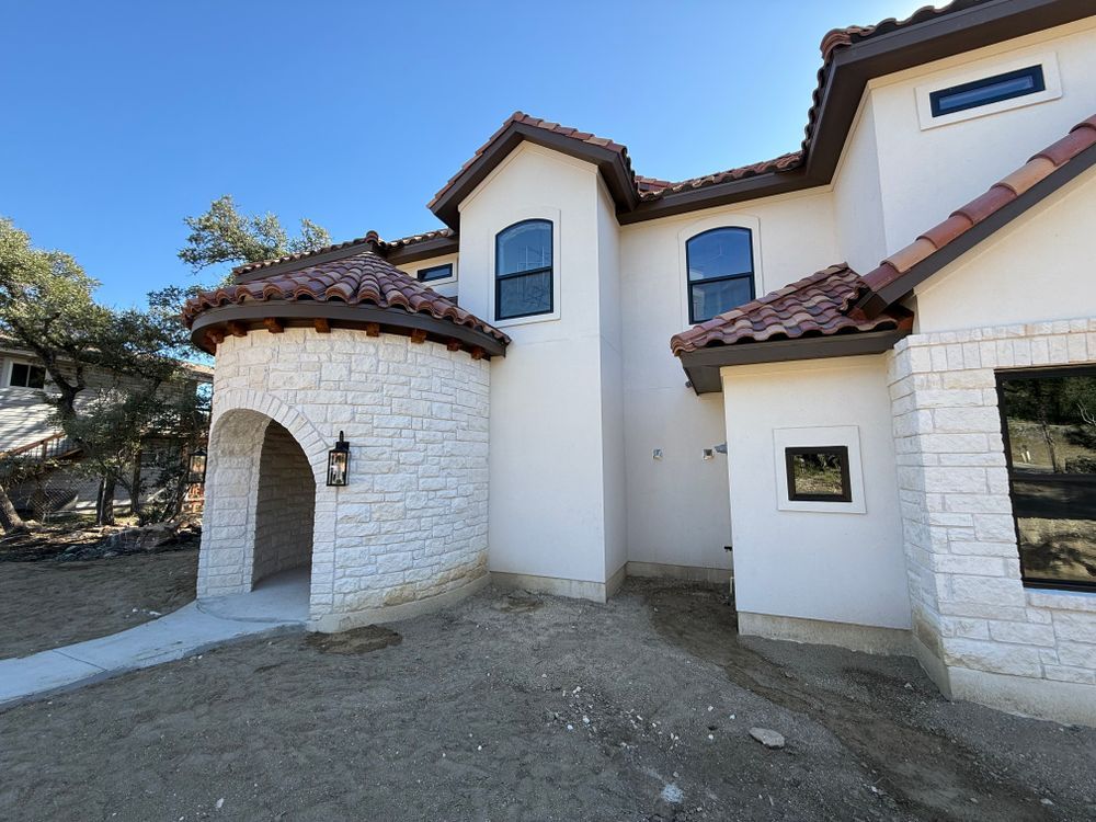 White stucco house with red tile roof, arched entryway, and small windows under a clear blue sky