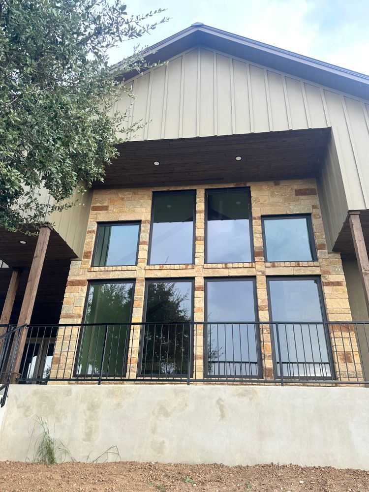 Two-story house facade with large windows, wood accents, and a black railing on a front balcony