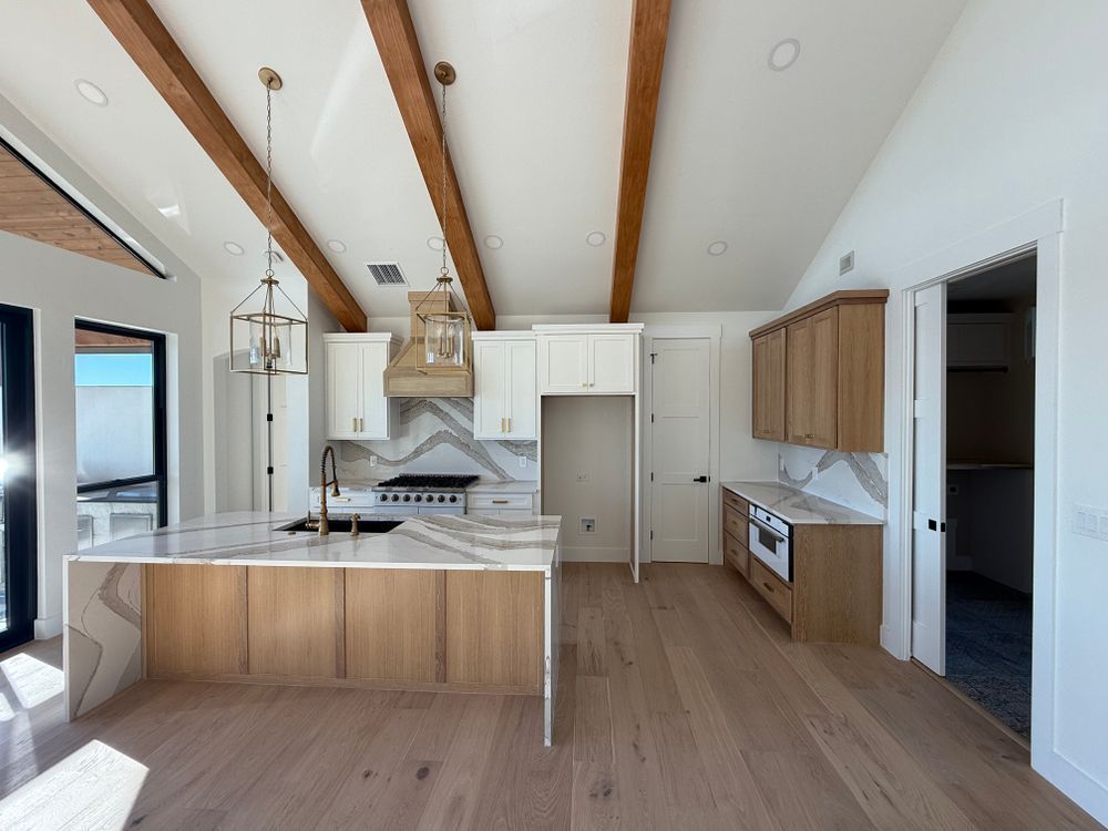 Bright modern kitchen with white cabinets, wood beams, island, and light wood floors