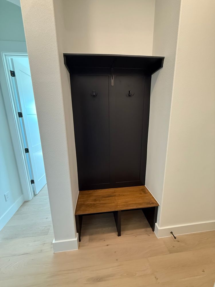 Built-in dark entry nook with coat hooks and wood bench in a light hallway