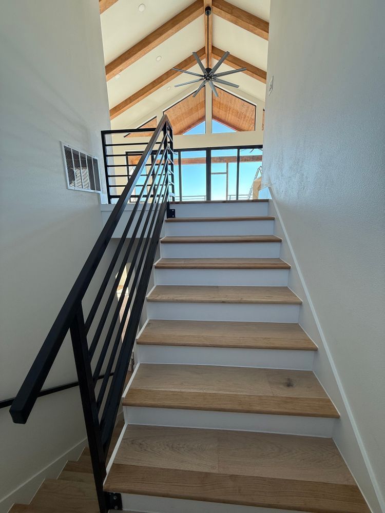 Staircase with black railing leading to a bright loft with exposed wooden beams.