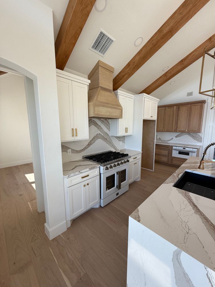 Modern kitchen with white cabinets, wood-beamed ceiling, stainless stove, and marble island counter.