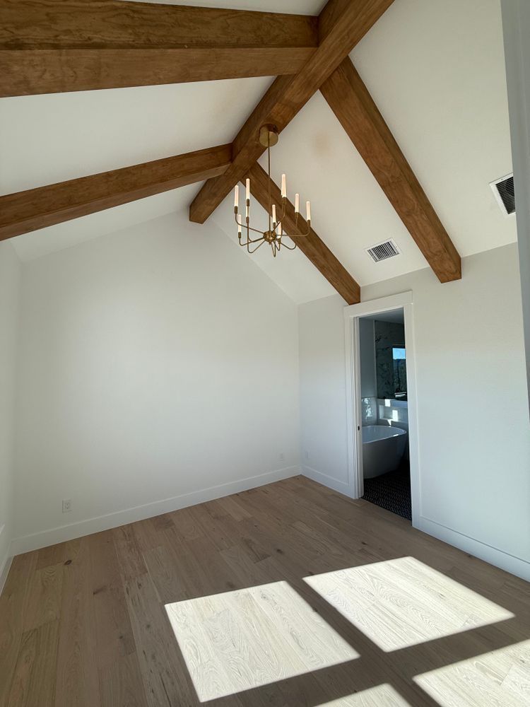 Empty white room with exposed wooden ceiling beams and sunlight casting window shadows on the floor.