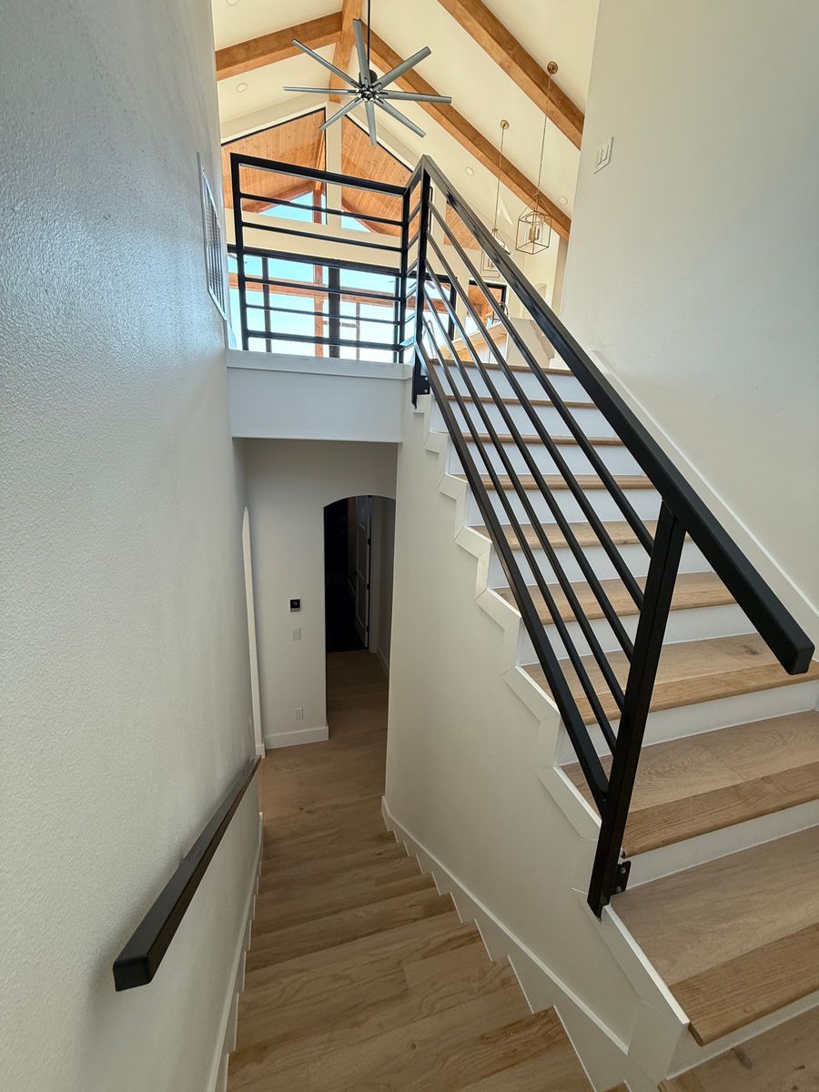Modern stairwell with wooden steps, black railing, white walls, and high vaulted ceiling with skylights