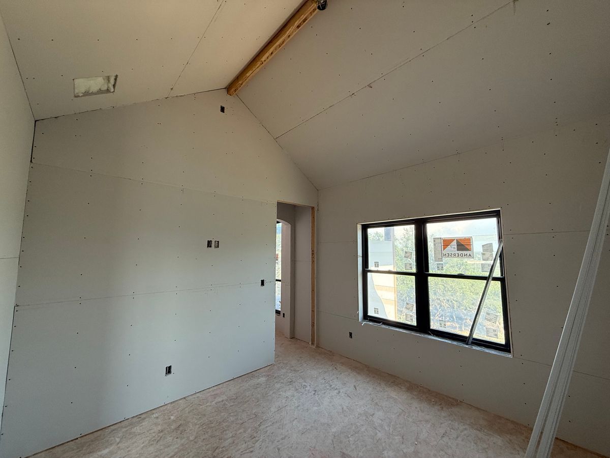 Empty unfinished room with white walls, sloped ceiling, and a window letting in daylight.