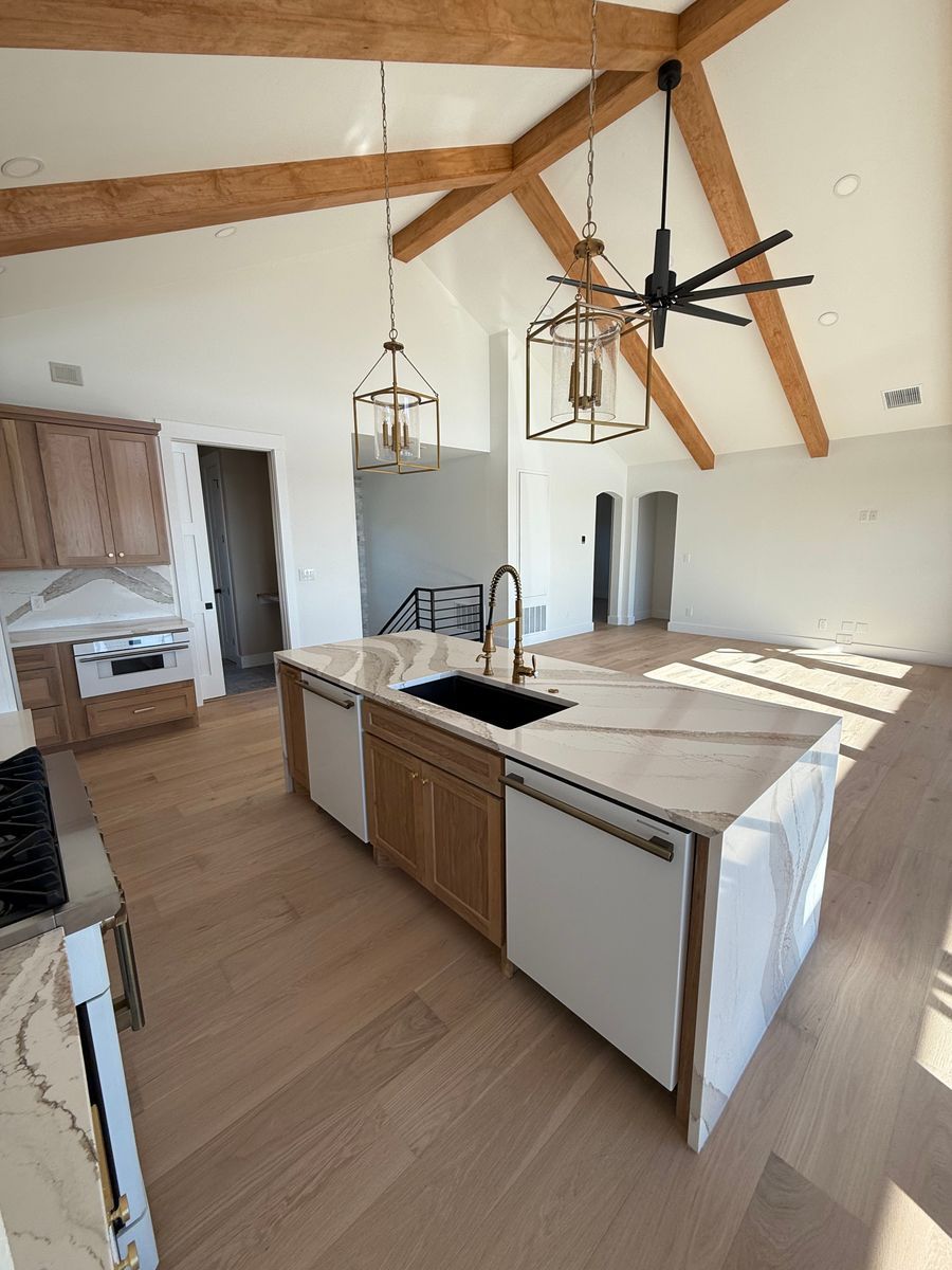 Modern kitchen with wood beams, white island, black pendant lights, and large fan ceiling.