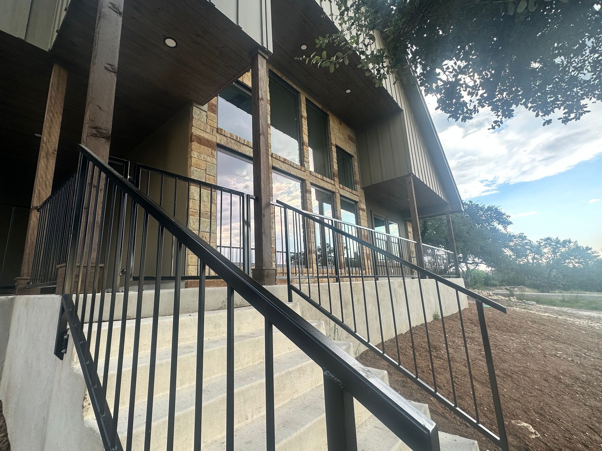 Brick building entrance with metal railings and steps beside a sunny landscape