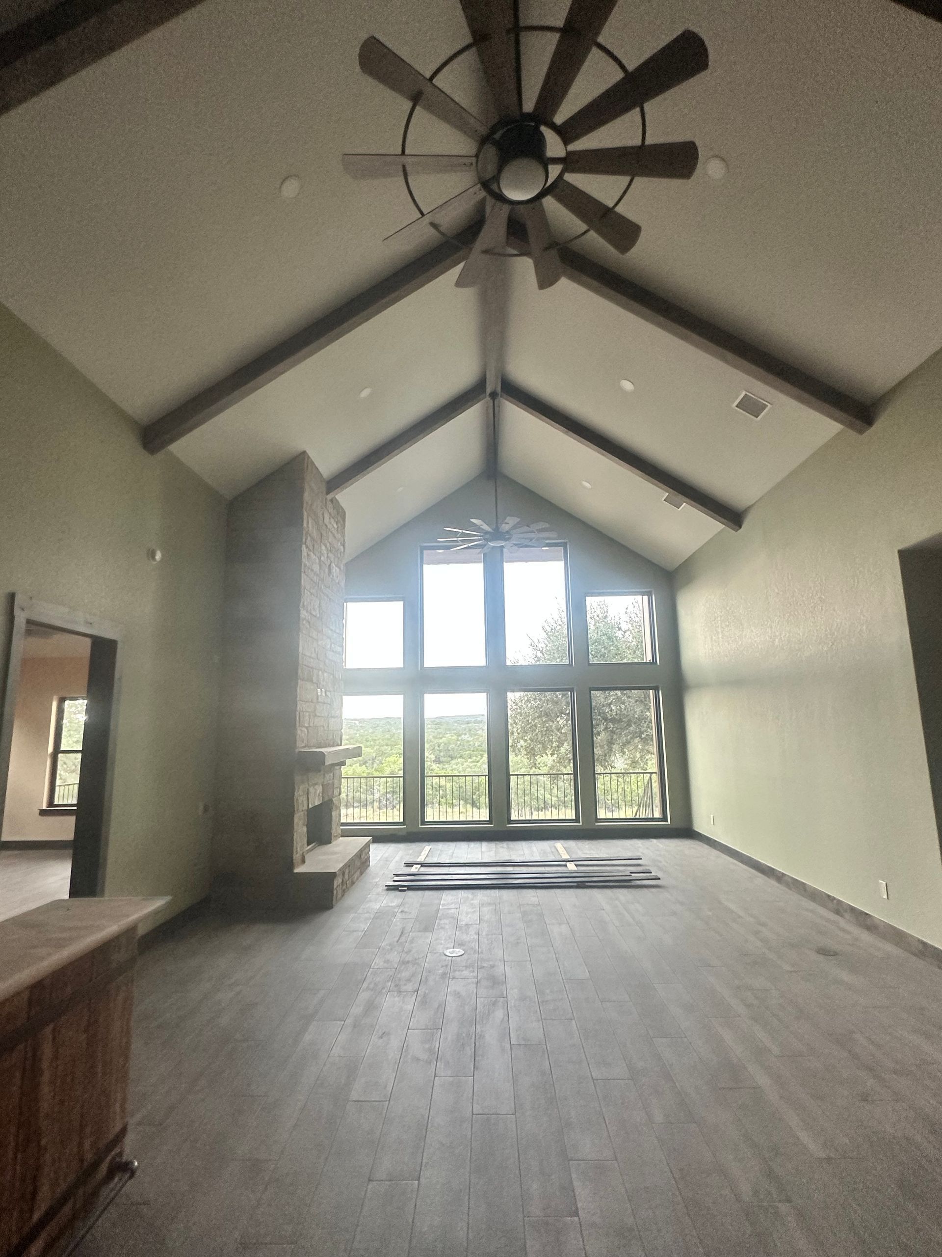 Empty living room with vaulted ceiling, large windows, and a ceiling fan.