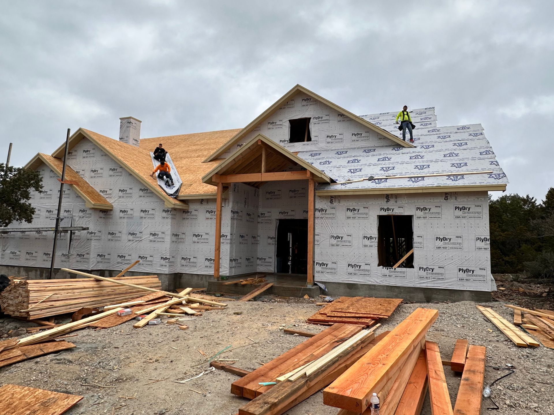 Two workers on a house roof during construction, with wood framing and materials in the foreground.