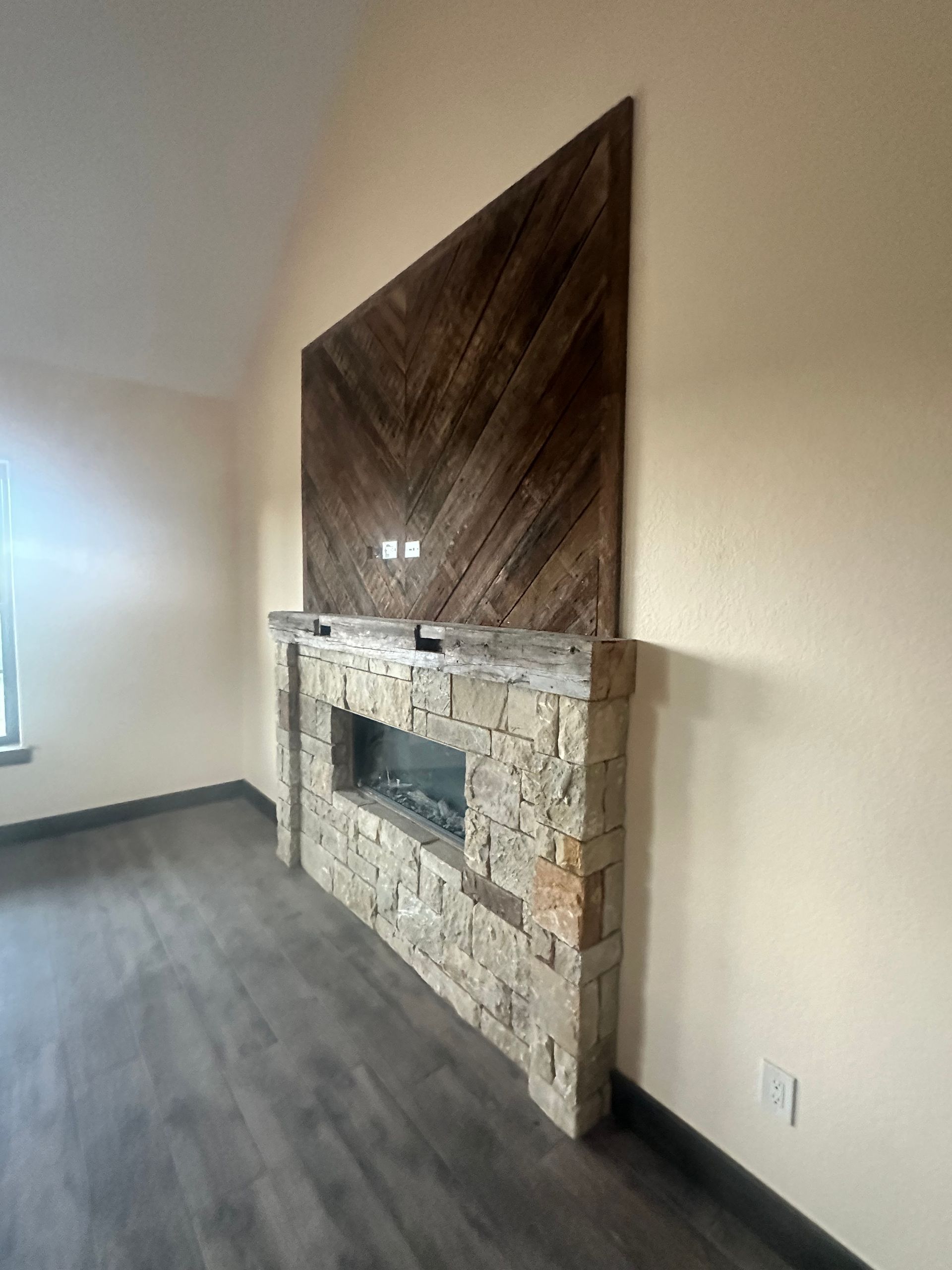 Empty living room with a stone fireplace and dark wood accent panel on the wall