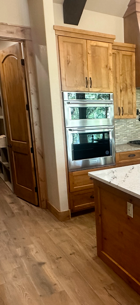 Wooden kitchen with stainless steel double oven, tall pantry cabinets, and a marble-topped island in the foreground