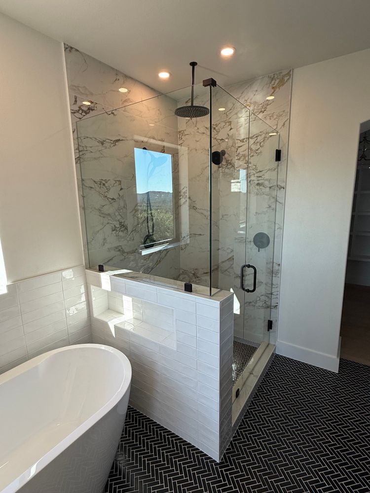 Modern bathroom with glass shower, white vanity wall, freestanding tub, and patterned dark floor rug