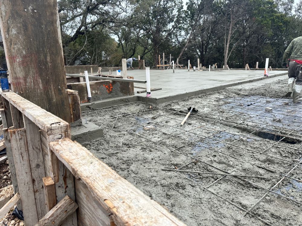 Construction site with wet concrete slab, wooden forms, and trees in the background