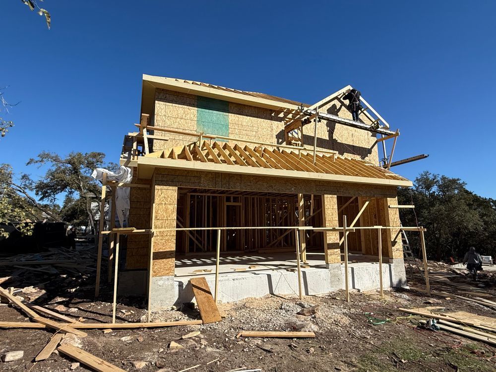 Partially built two-story house with exposed wood framing and scaffolding on a sunny construction site
