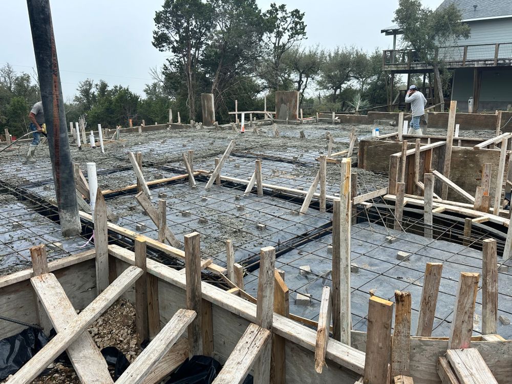 Concrete foundation under construction with wooden formwork and rebar, workers in the background outdoors