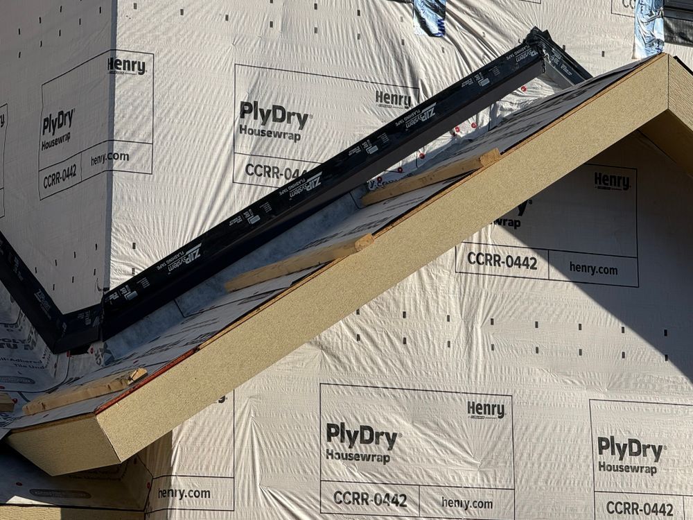Roof framing with angled wooden beam over house wrap and black flashing under construction