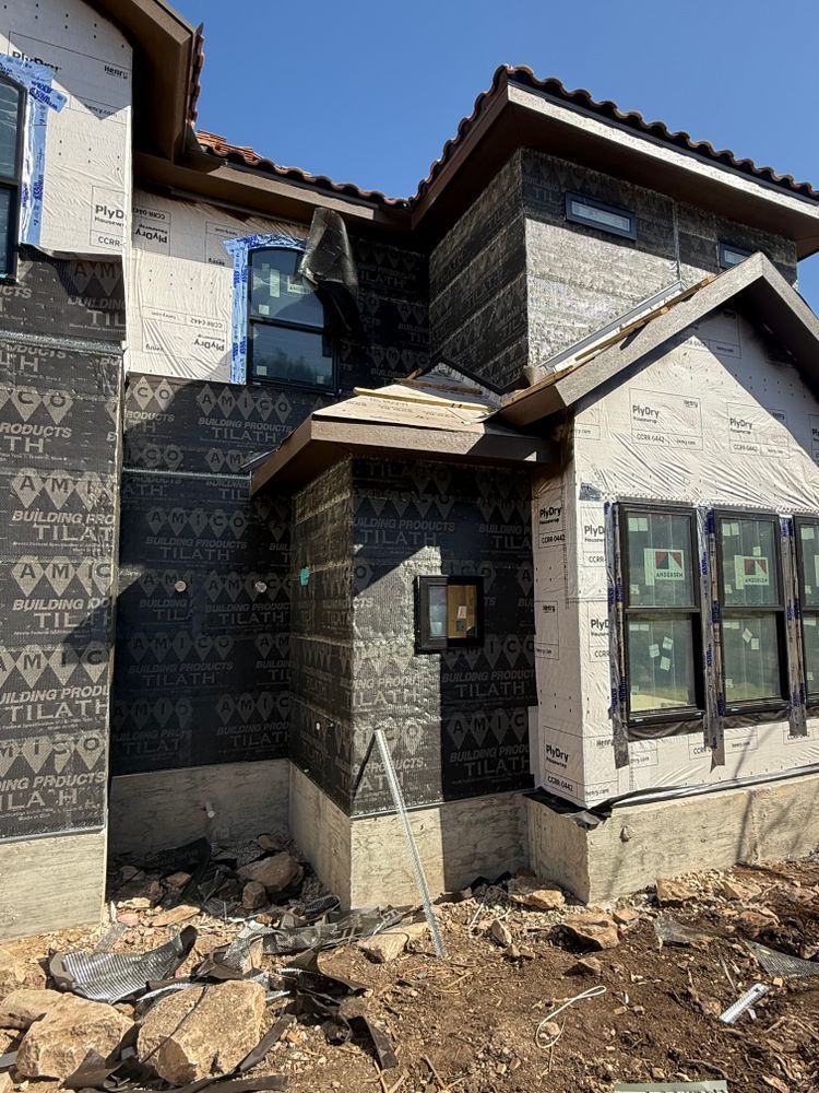 Partially built house with stucco walls, dark roof tiles, and exposed dirt in front