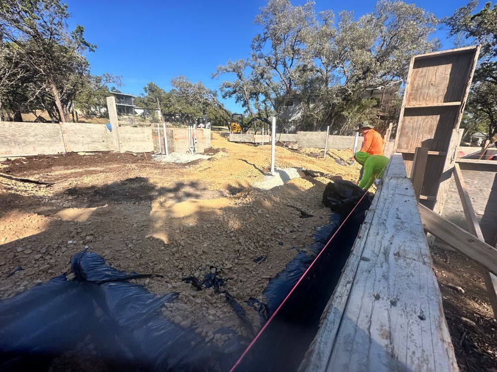 Person in orange shirt working on a dirt construction site beside a long concrete wall.