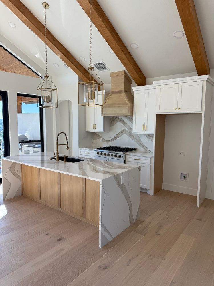 Modern kitchen with marble island, white cabinets, exposed wood beams, and stainless appliances