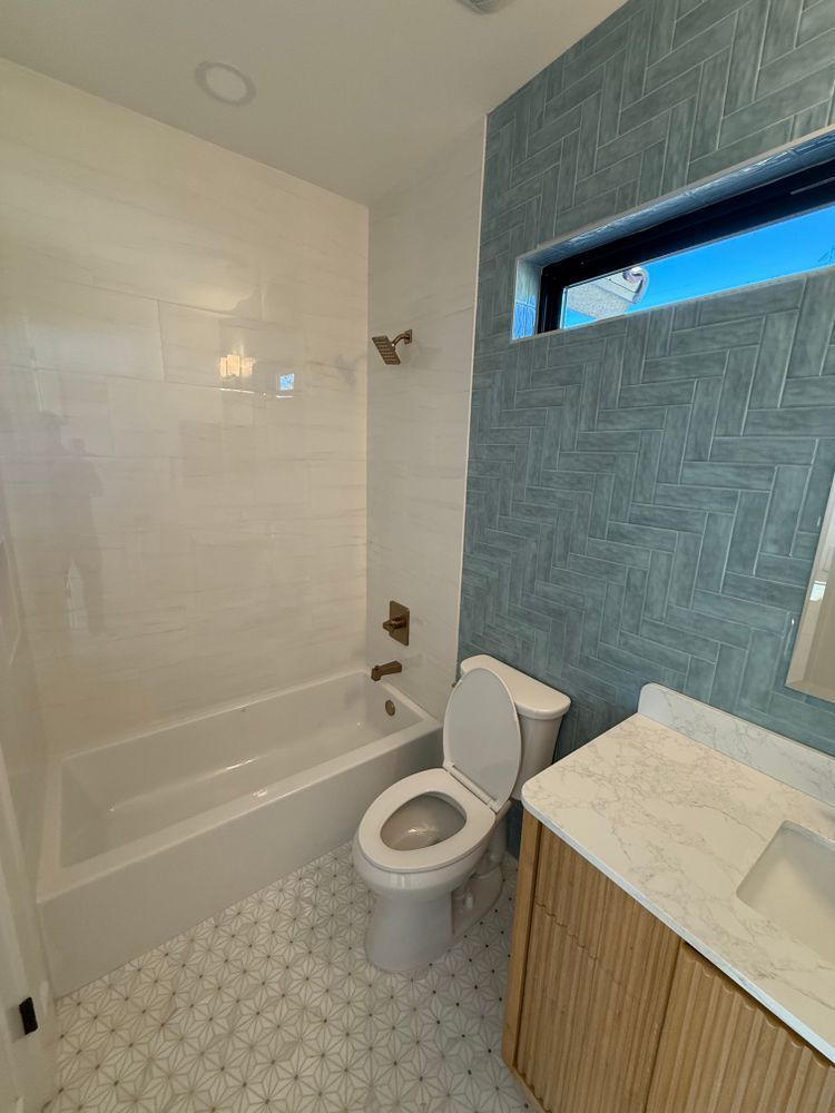 Small bathroom with tub, toilet, white vanity, patterned blue wall, and frosted window.