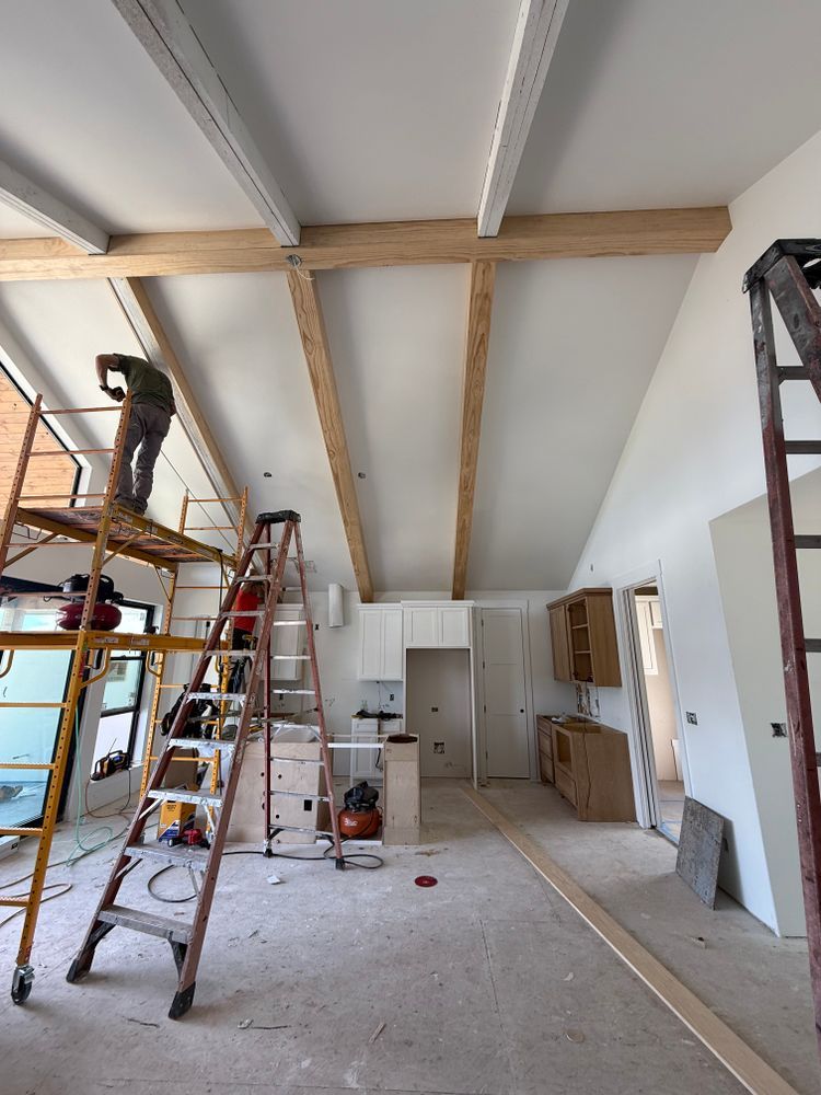 Renovation room with ladders, exposed ceiling beams, tools, and unfinished drywall during construction