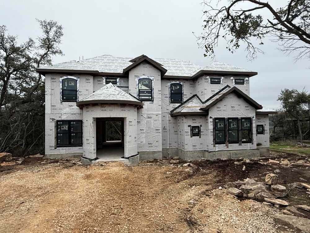 Unfinished two-story house with stone facade and dirt front yard under a gray sky