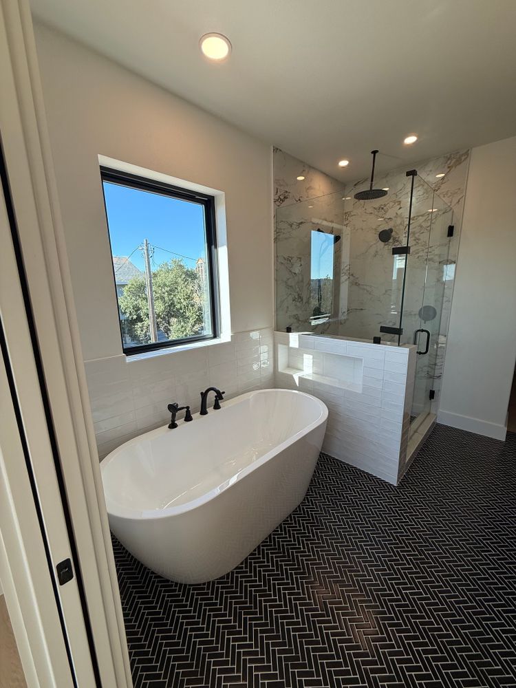 Modern bathroom with freestanding tub, glass shower, and black patterned floor tiles