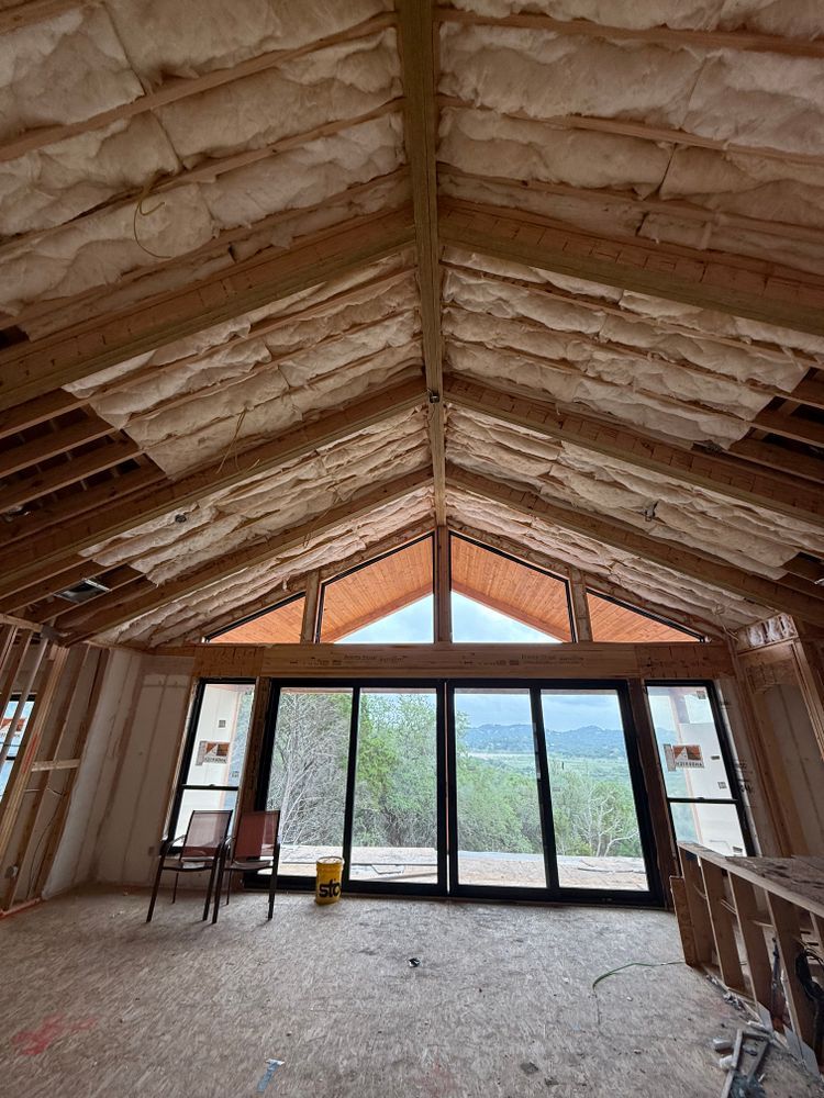 Unfinished attic room with exposed insulation, bare floor, and large glass doors overlooking hills.