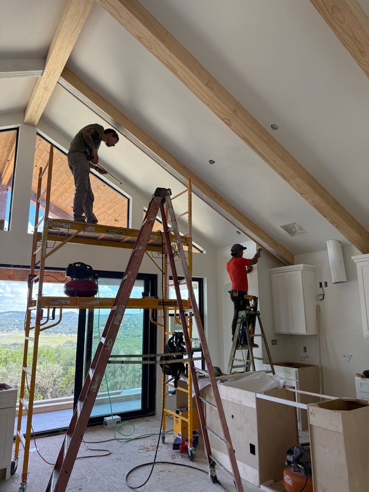 Workers installing ceiling beams in a bright room with ladders and tools.