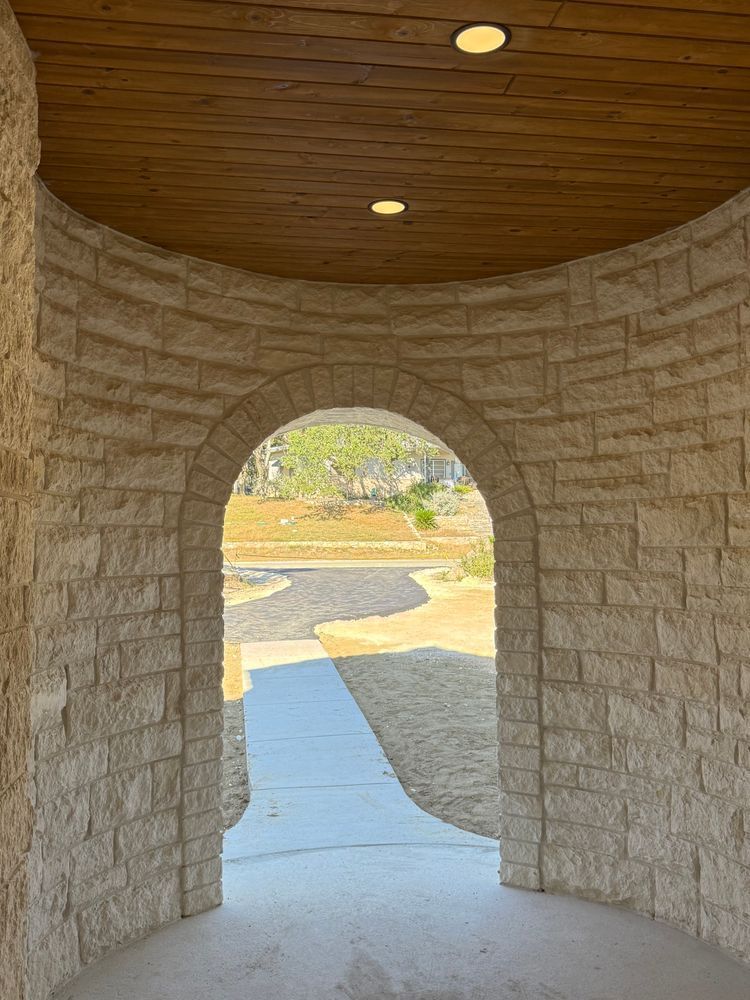 Stone archway hallway with a wooden ceiling, leading to a sunlit path outside